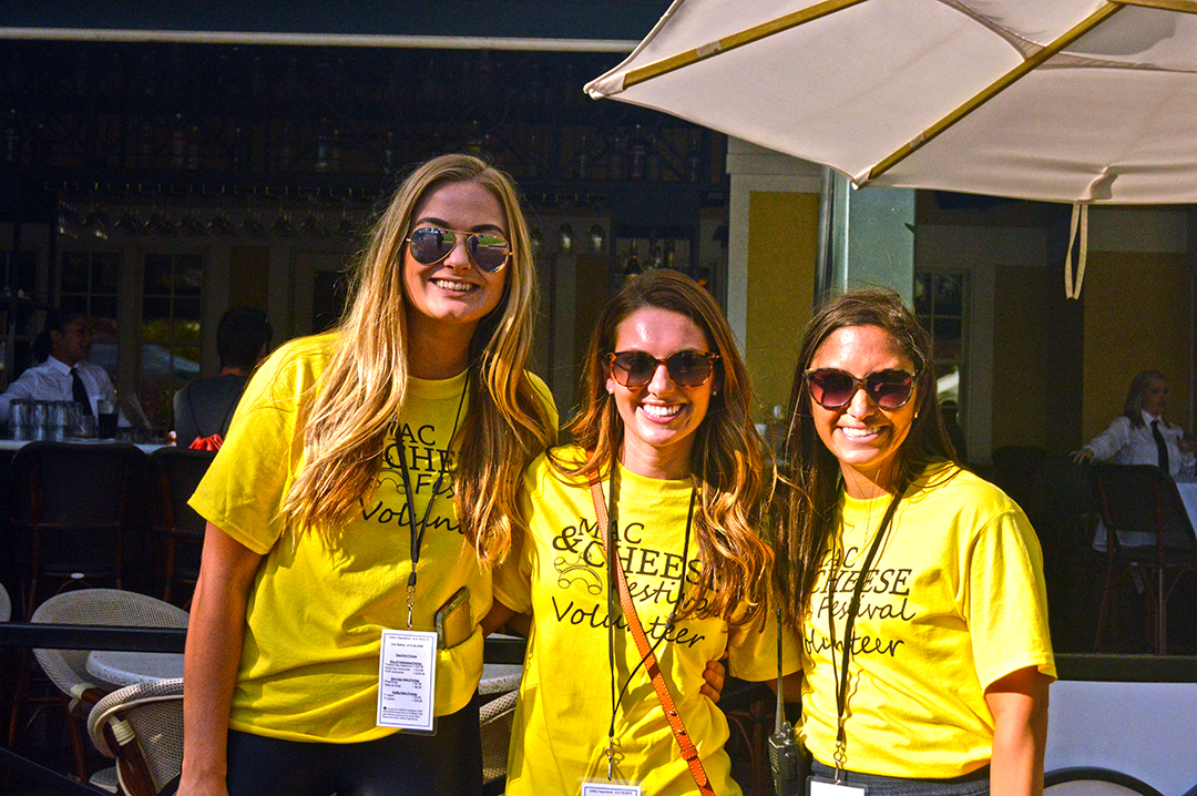 Three women dressed in yellow t-shirts posing in front of Brio at Mac and Cheese Fest